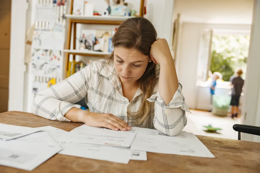 Eine Frau sitzt vor einem Stapel Rechnungen und ist verzweifelt, sie benötigt finanzielle Überbrückungshilfe.