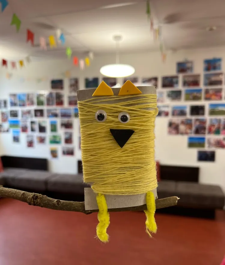 Kinder haben aus einer Kartonrolle eine gelbe Eule gebastelt.